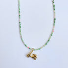 Necklace with green and pink beads and a gold charm on a light blue background