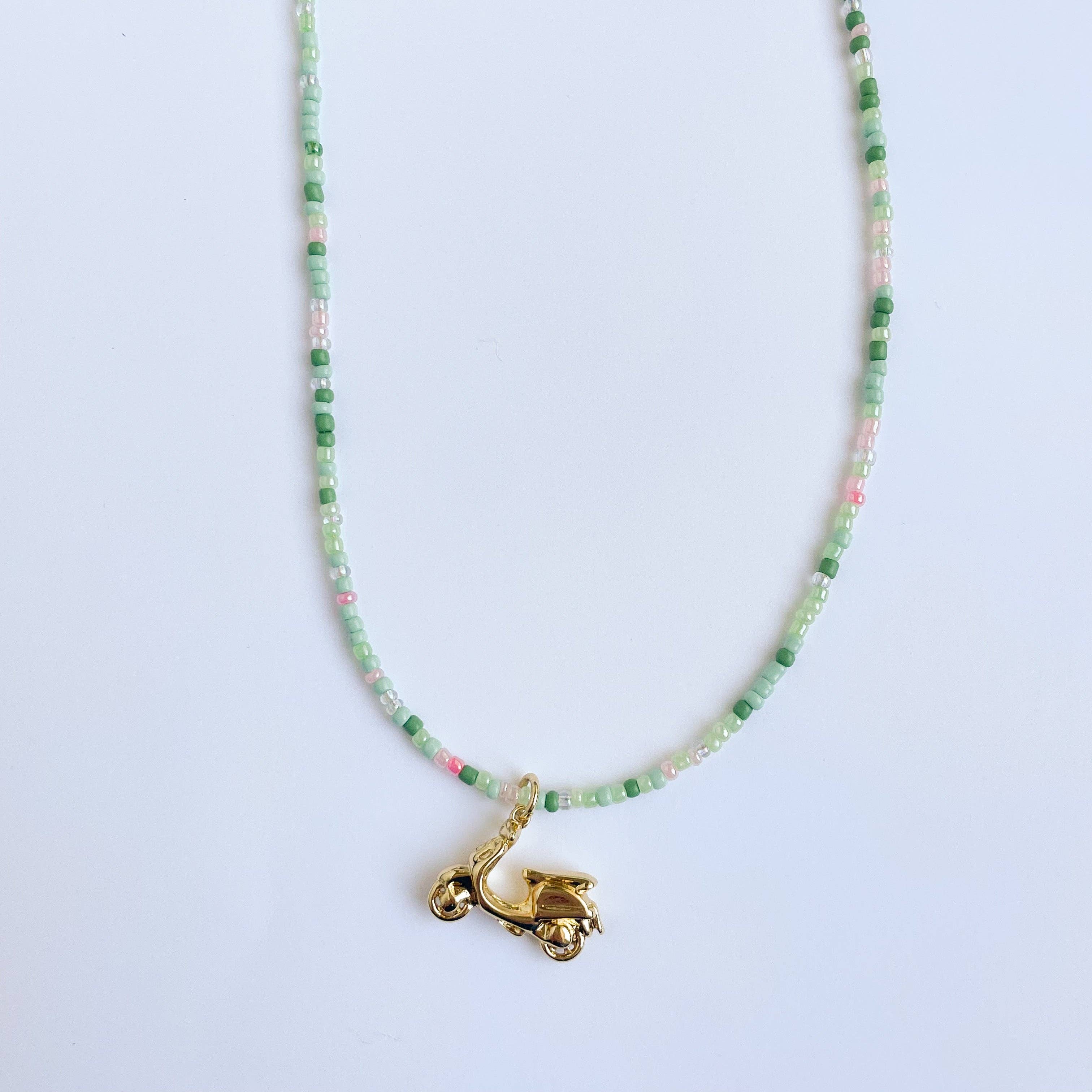 Necklace with green and pink beads and a gold charm on a light blue background