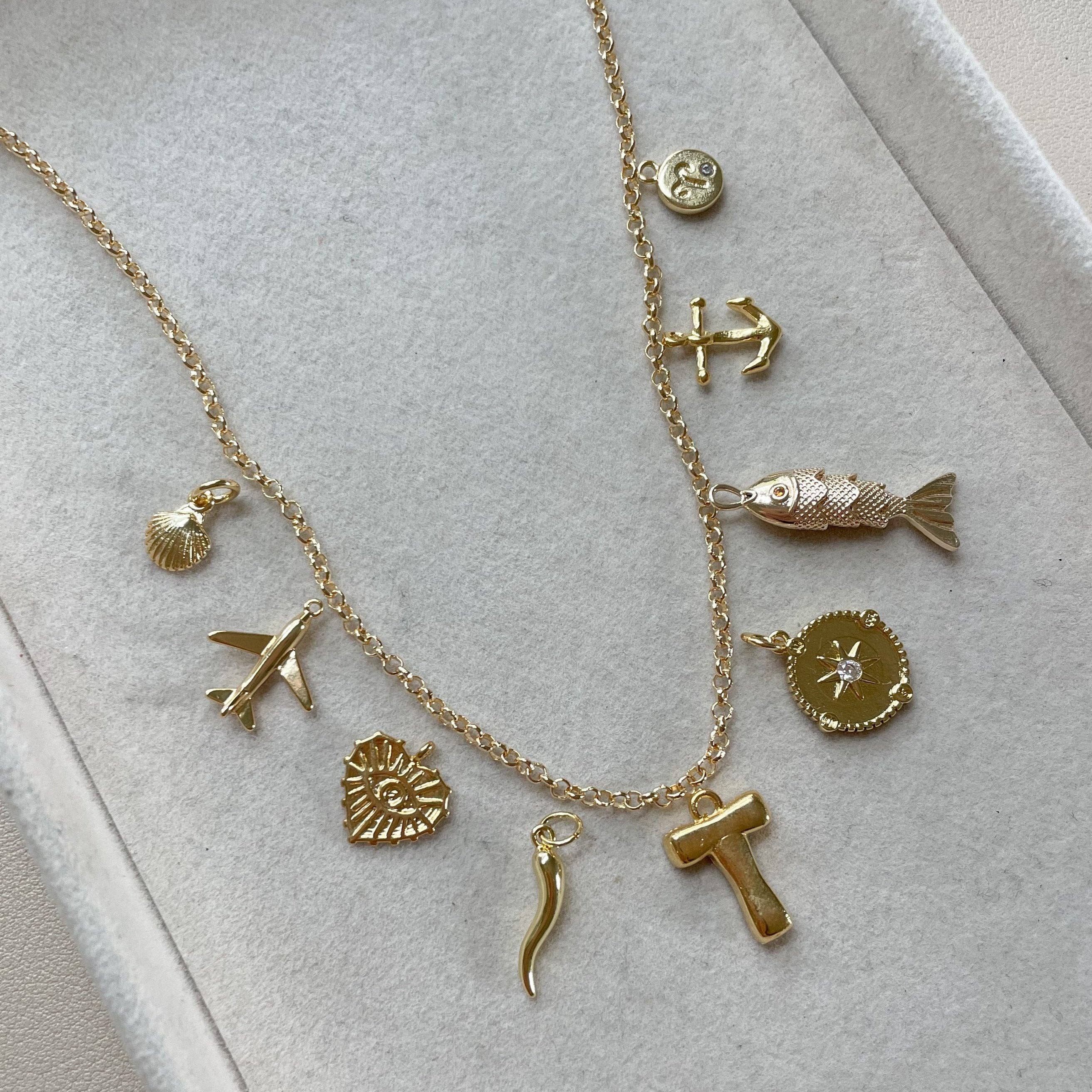 Gold necklace with various charms on a light gray surface