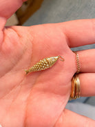 Gold fish-shaped pendant held in a hand with a blurred background