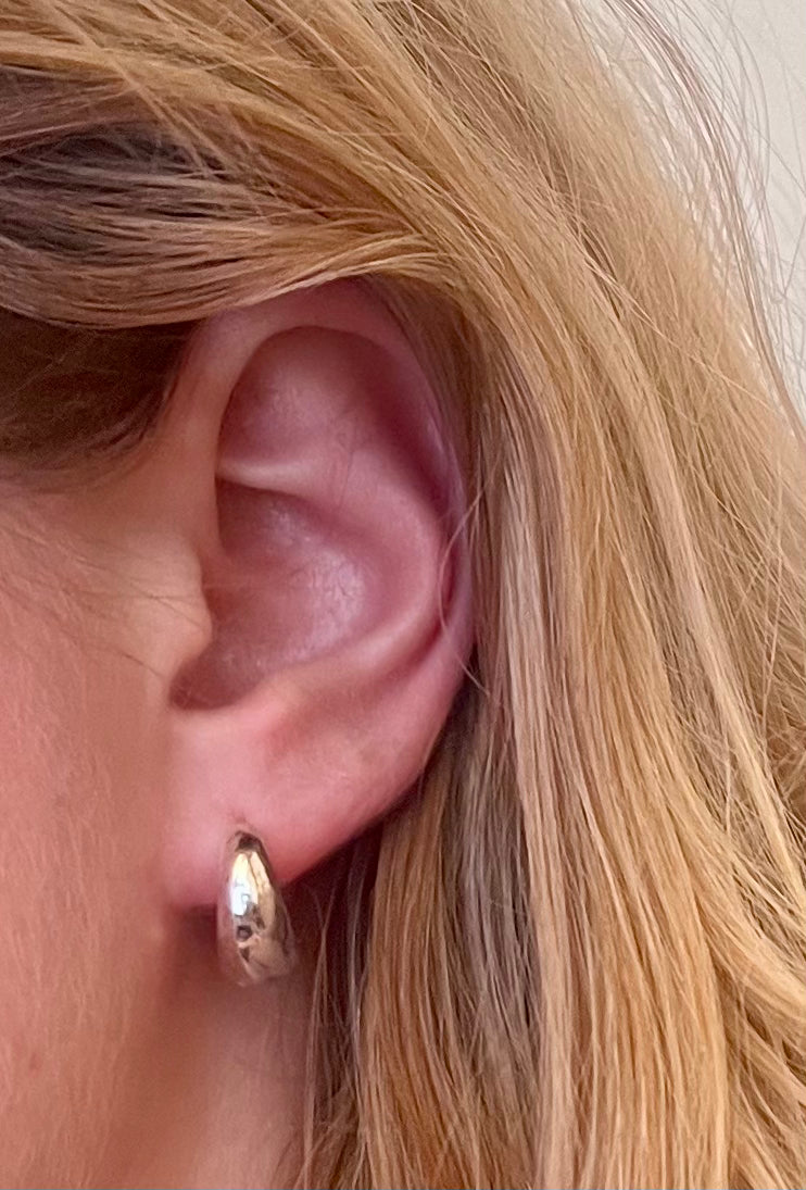 Close-up of an ear wearing a silver hoop earring with blonde hair.