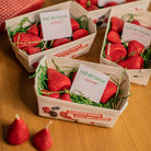 Small cardboard boxes with red strawberry candles and a card on a wooden surface