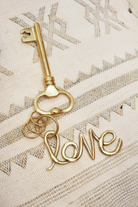 Gold key-shaped charm with 'love' on a textured beige background