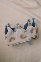 A handcrafted children's crown with a blue and multicolor pattern, featuring small pompons.